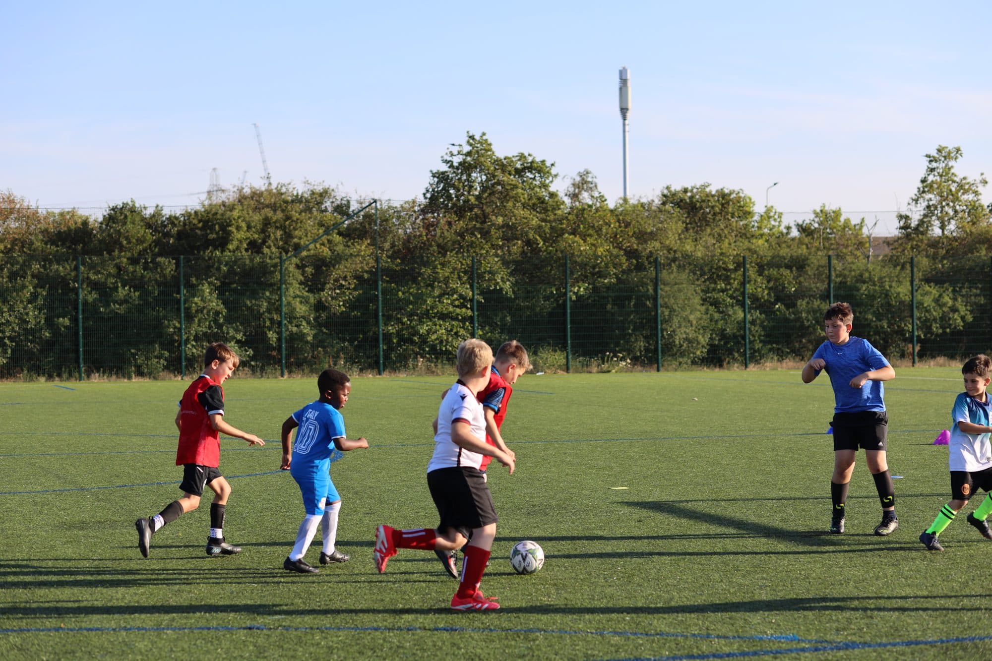 Players attack towards goal during a game on a sunny artificial pitch