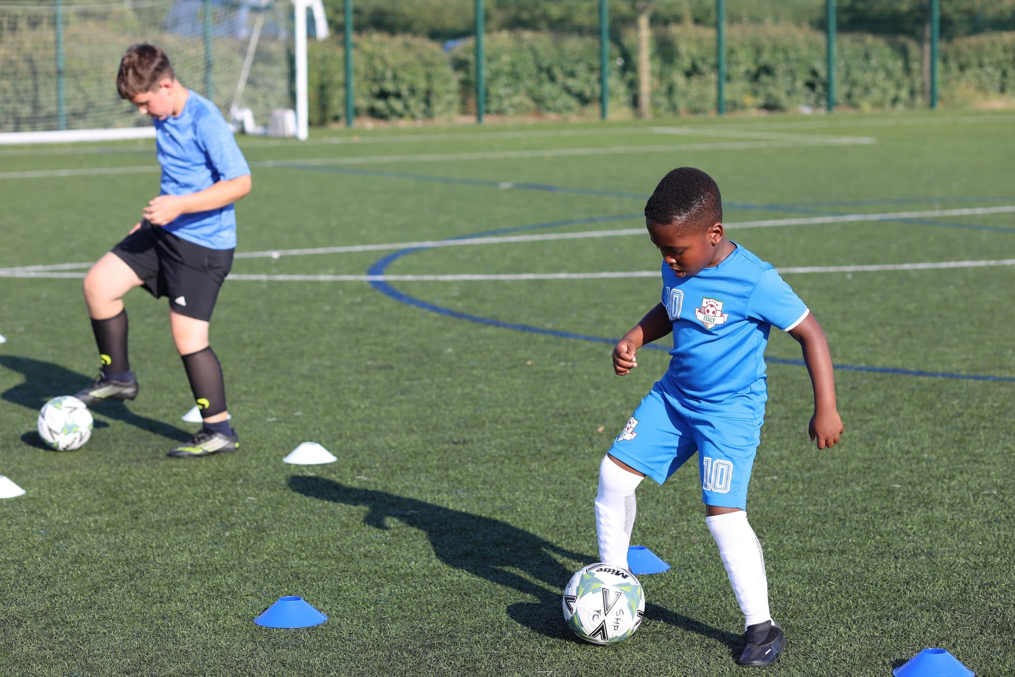 Two players in blue keep the ball close as they move around cones