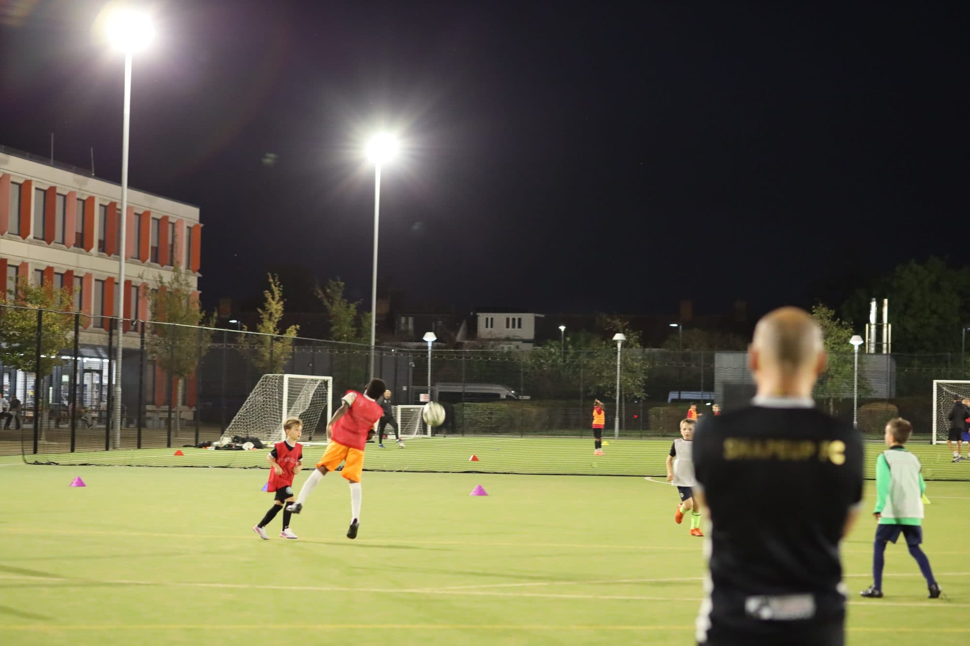 A ShapeUp FC coach watches a game under the floodlights