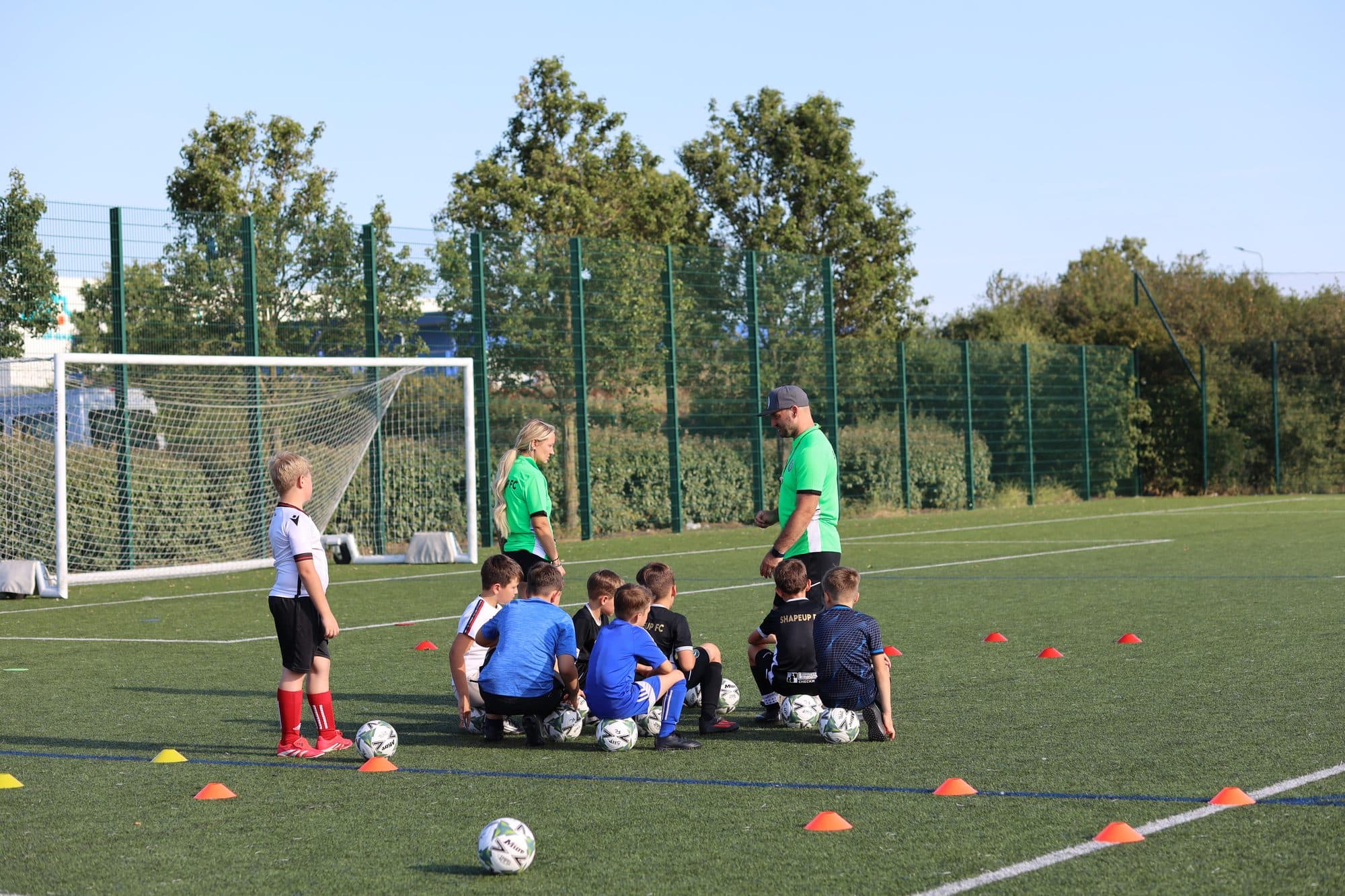 Two coaches gather a group of young players for a team talk beside the goal on a sunny evening