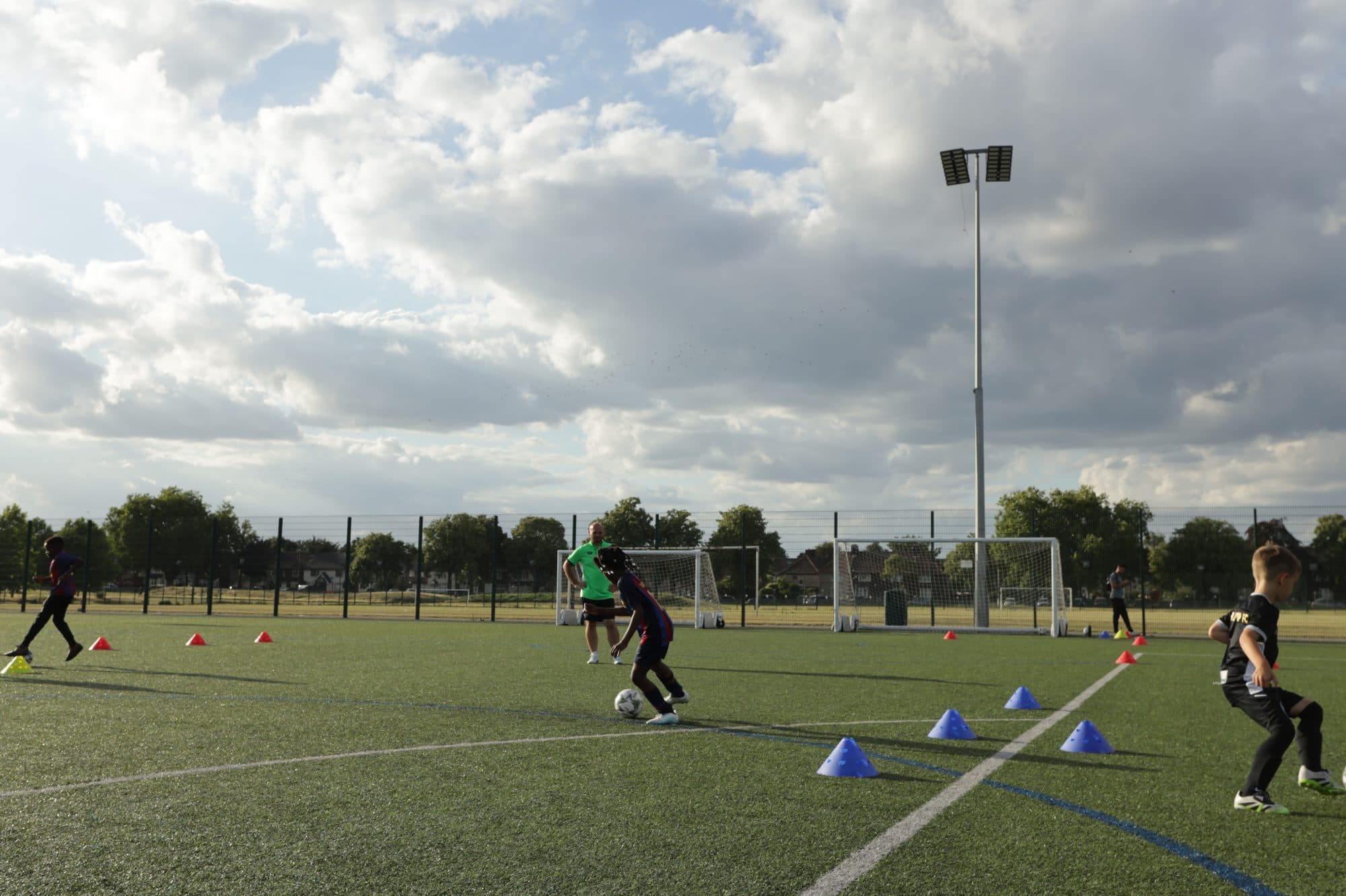 Players work through a cone drill under dramatic clouds and a floodlight