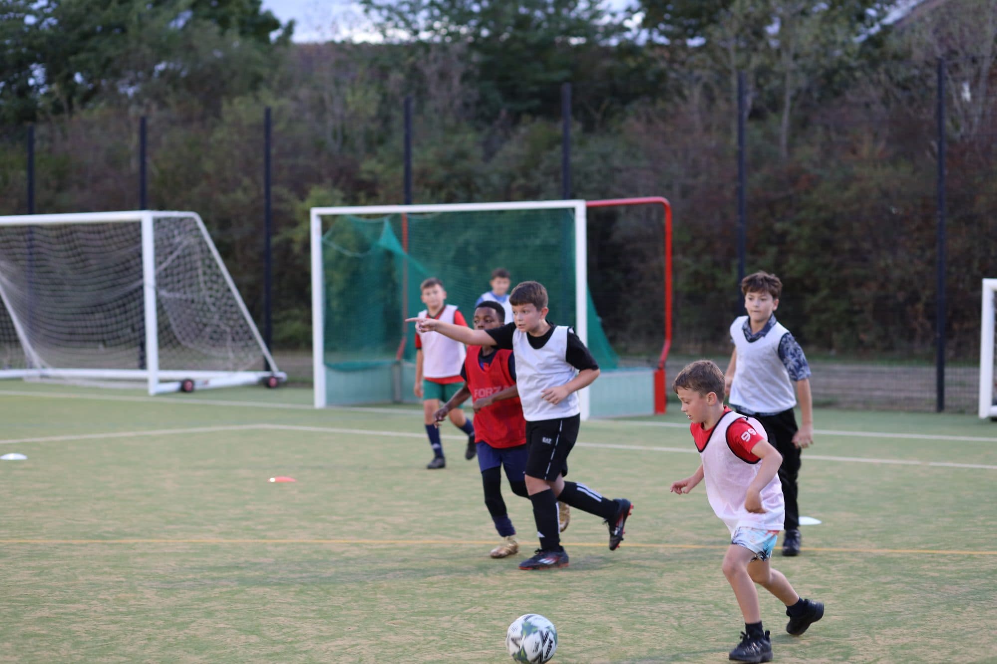 Players in white and red bibs compete in an evening game in front of the goals