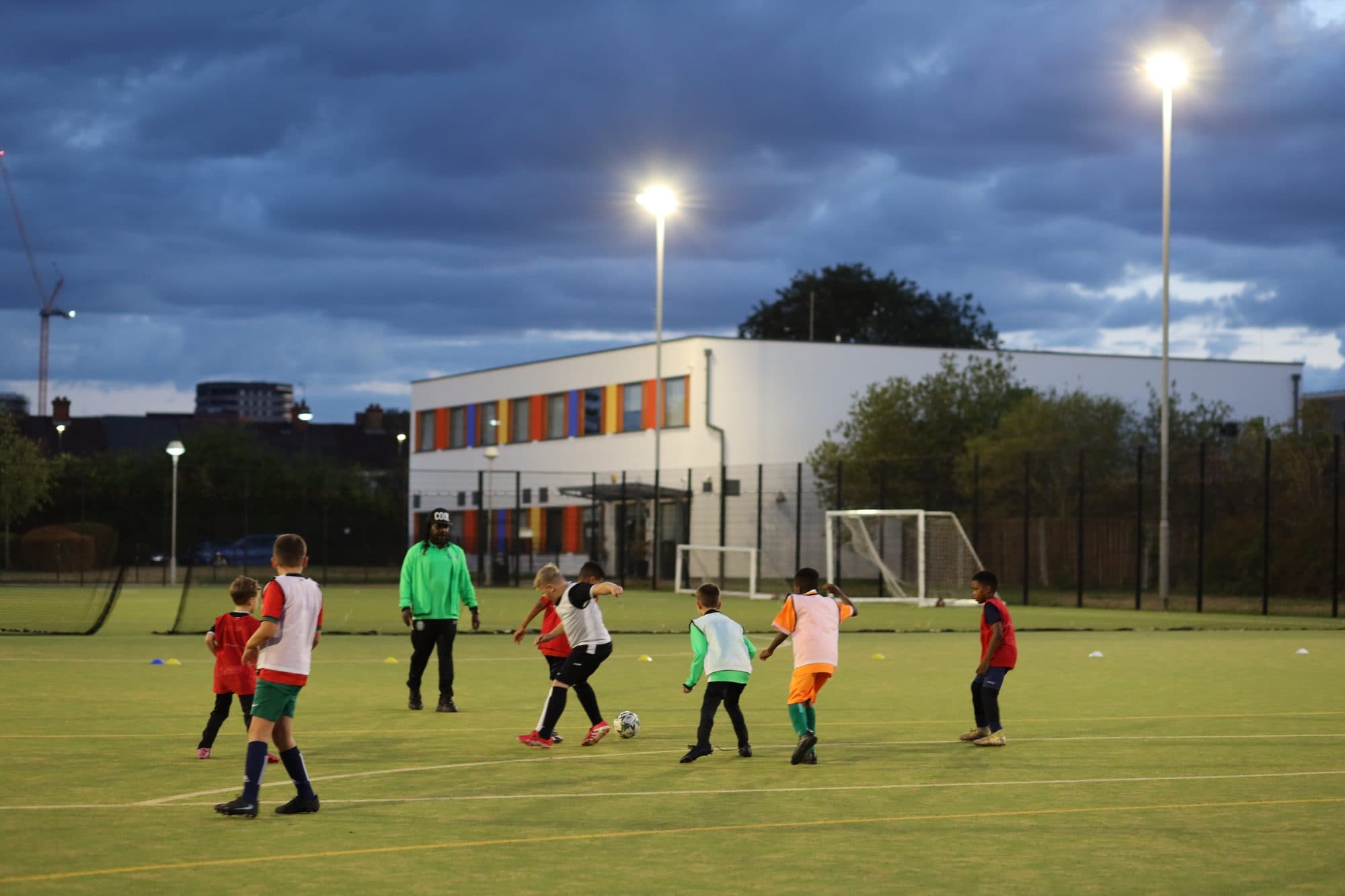 A wide view of a game under the floodlights at dusk, with coaches watching