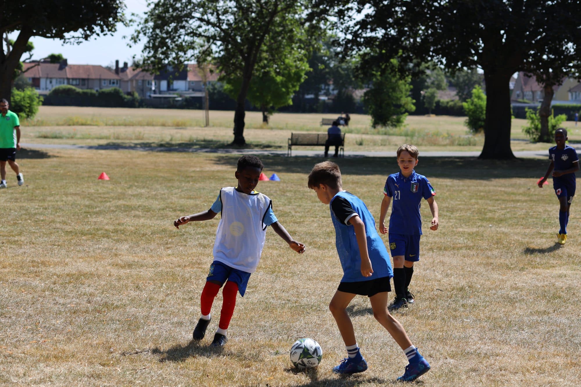 A player in a blue shirt shields the ball from an opponent in a white bib