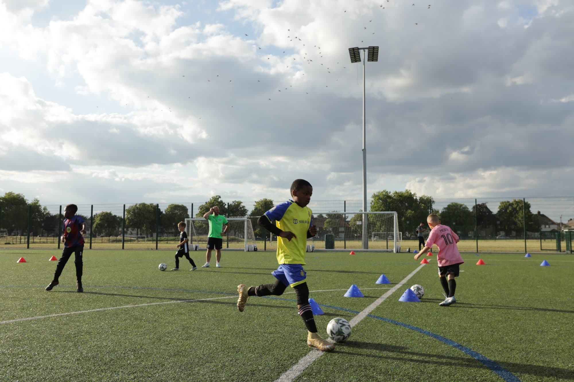A player in yellow kicks the ball across the artificial pitch