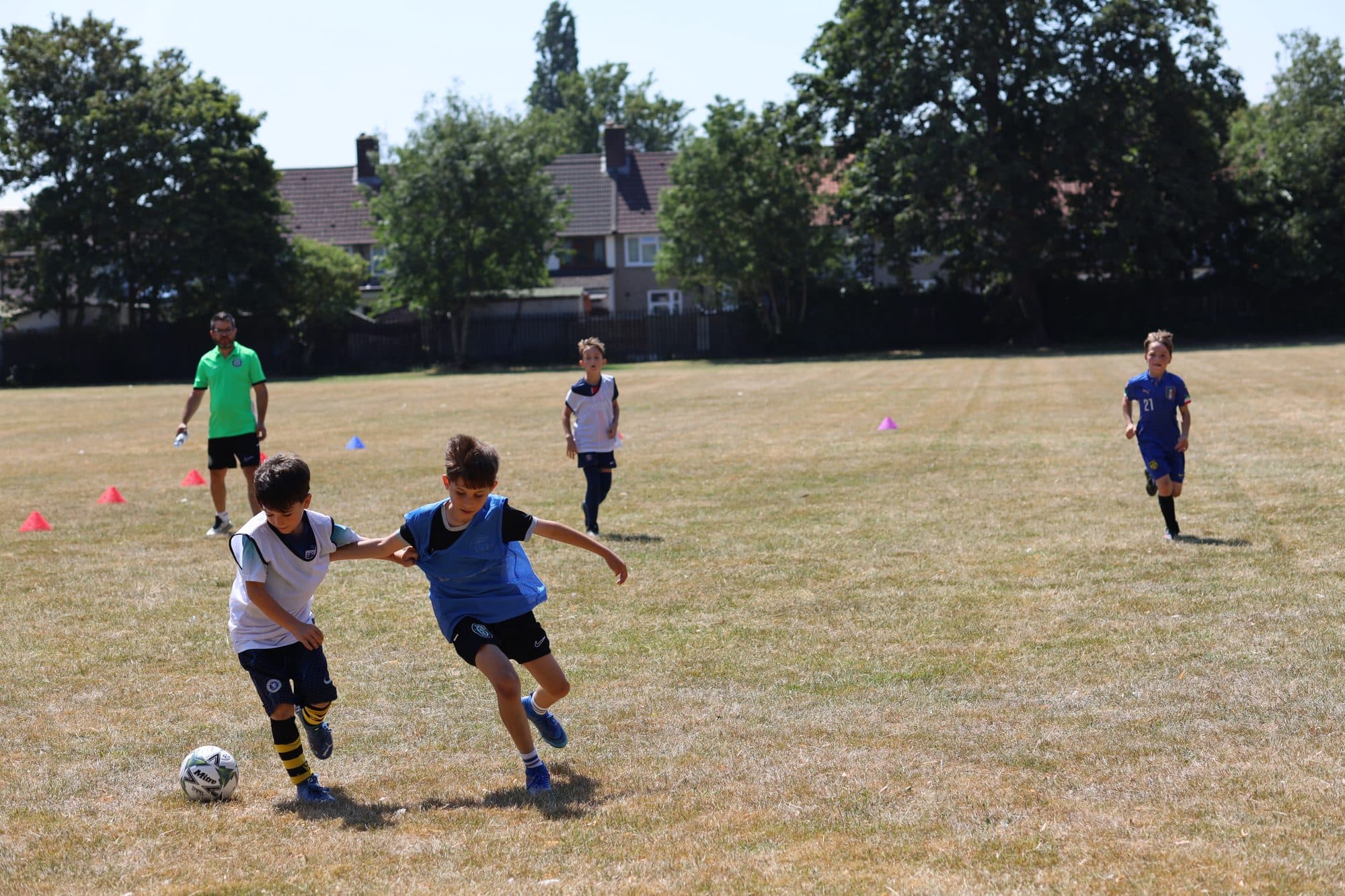 Two players go shoulder to shoulder for the ball while a coach watches
