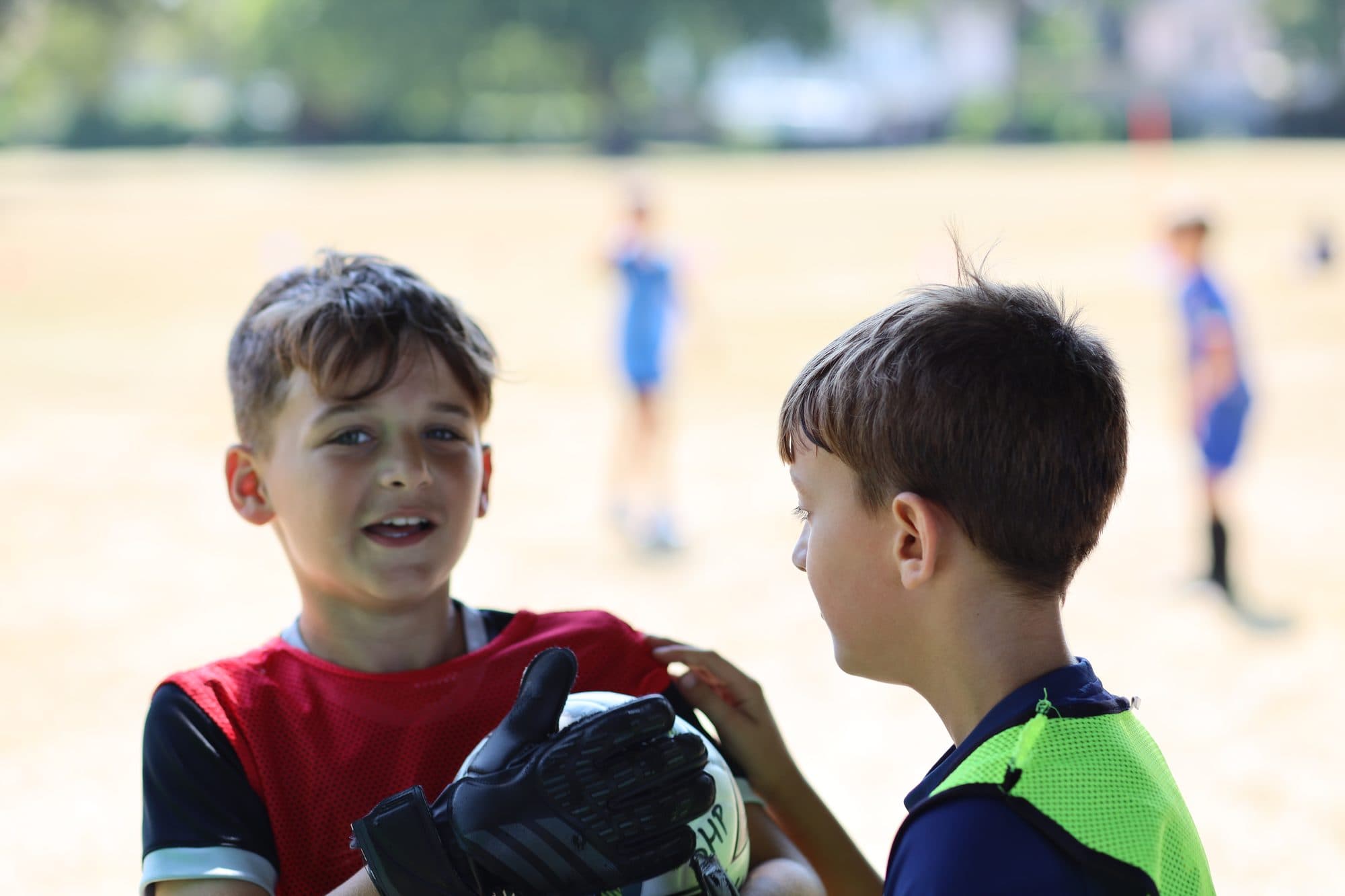 A young goalkeeper in gloves smiles at a teammate on a sunny day