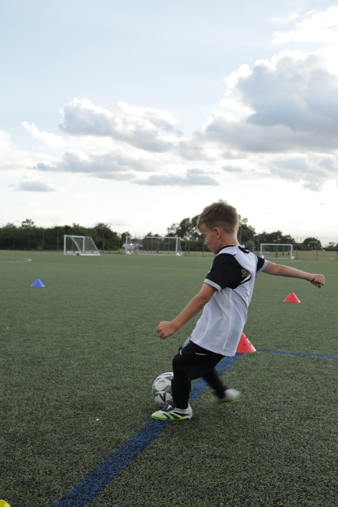 A young player in a white bib follows through after kicking the ball