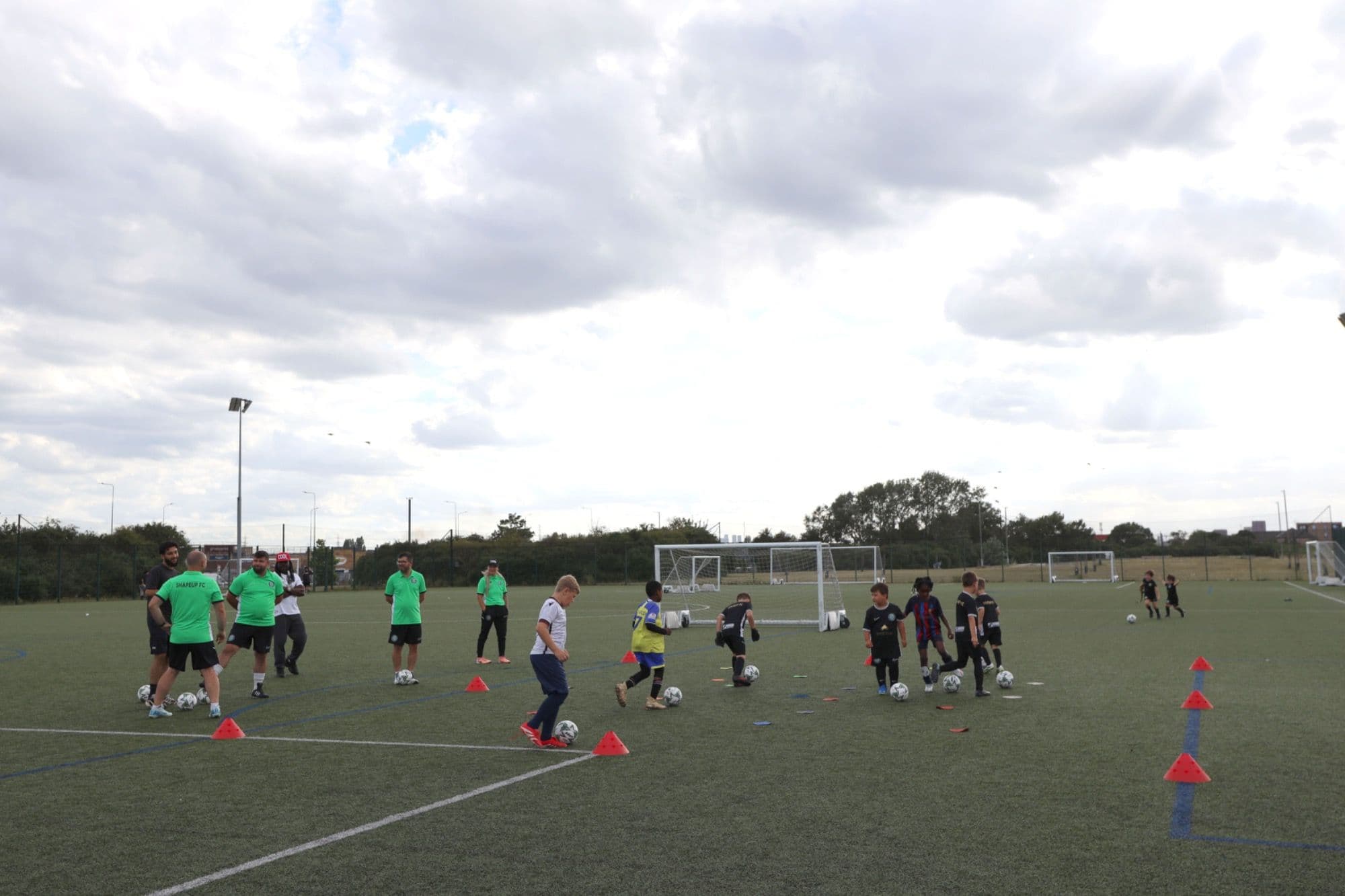 A youth training session on a floodlit artificial pitch with coaches in green tops