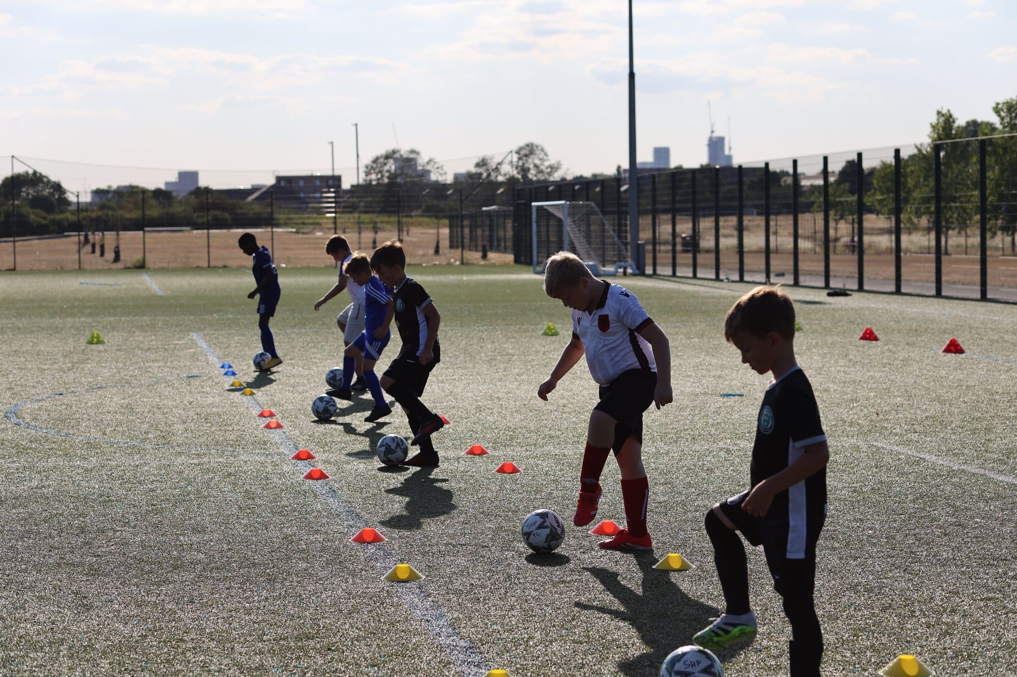 Players practise ball mastery in a line as the low evening sun casts long shadows