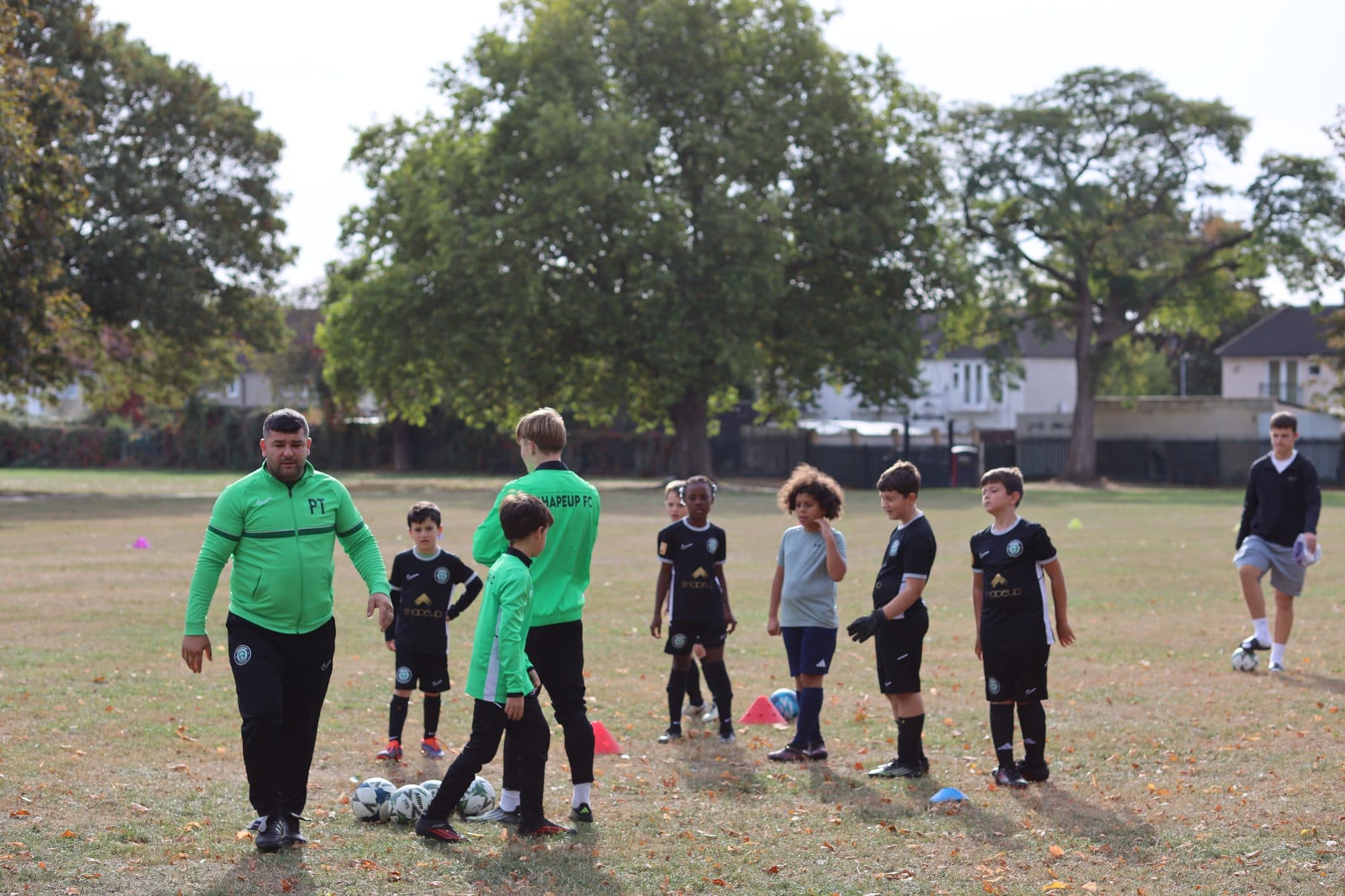 Coaches in green talk to a group of young players in the park on an autumn day