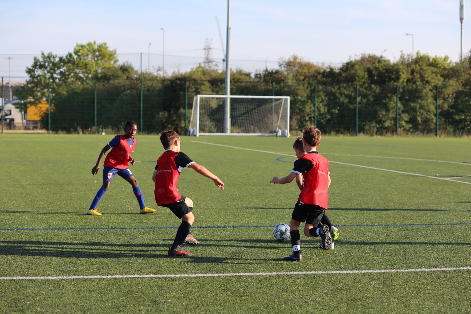 Three players in red and black battle for the ball during a small-sided game on an artificial pitch